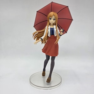 May include: A figurine of a female anime character holding a red umbrella. She wears a white jacket, a dark blue top, a red skirt, and black tights. The figure stands on a clear circular base.