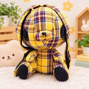 May include: A plush rabbit toy featuring a yellow and purple plaid fabric pattern. The stuffed animal has large, smooth black oval eyes, a small black nose, and long, floppy ears. The feet are solid black, and the body is constructed from multiple fabric panels.