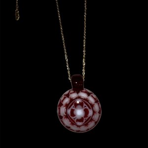 May include: A red and white glass pendant necklace with a detailed floral design. The pendant is round and hangs from a gold chain.