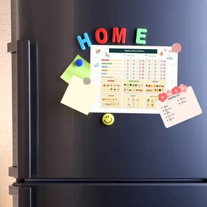 May include: A black refrigerator with a white magnetic chart titled "Mighty Munch Meter" with a grid for tracking food intake. The chart includes images of fruits, vegetables, grains, and dairy. There are also colorful magnetic letters spelling "HOME" and a smiley face magnet.