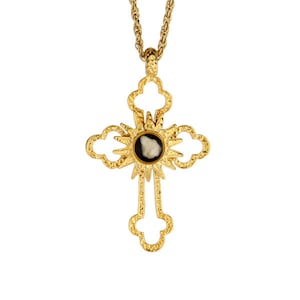 May include: A gold cross pendant necklace with a black and white cameo in the center. The cross is ornate and has a sunburst design around the cameo.