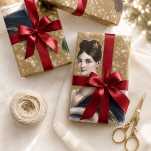 K&ouml;nnte beinhalten: Rechteckige Geschenkboxen in goldfarbenem Papier mit Sprenkelmuster, verziert mit dem Portr&auml;t einer Person mit dunklem Haar und einem Stern-Accessoire. Jede Box ist mit einer dunkelroten Satinschleife gebunden. Dazu liegen beiges Garn und eine goldene Schere.