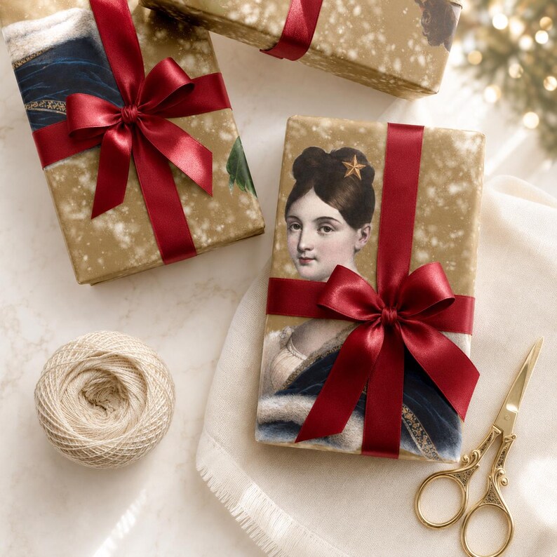 K&ouml;nnte beinhalten: Rechteckige Geschenkboxen in goldfarbenem Papier mit Sprenkelmuster, verziert mit dem Portr&auml;t einer Person mit dunklem Haar und einem Stern-Accessoire. Jede Box ist mit einer dunkelroten Satinschleife gebunden. Dazu liegen beiges Garn und eine goldene Schere.