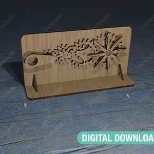 以下が含まれることがあります： 歯車模様のついた木製スタンド。スタンドは薄い茶色の木でできており、前面に歯車模様が施されています。歯車は金属製で黒く塗られています。スタンドの高さは約25cm、幅は約15cmです。