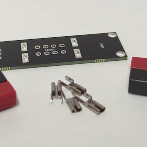 May include: A black circuit board with the text "F8001" and "DC24-12" printed on it. The board is surrounded by two red and black connectors and several silver metal connectors.