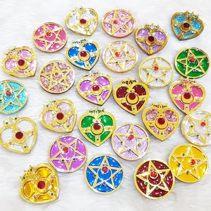 Könnte beinhalten: Eine Sammlung von 24 goldfarbenen, herzförmigen und sternförmigen Dekorationsanhängern mit bunten Emaille- und Glitzerakzenten. Die Anhänger zeigen eine Vielzahl von Designs, darunter Herzen, Sterne und andere geometrische Formen.