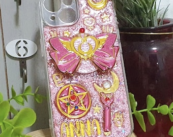 Può includere: Una cover per telefono trasparente riempita di glitter rosa, caratterizzata da un grande fiocco rosa e oro, un ciondolo a forma di stella con gemme colorate, uno scettro a mezzaluna e il nome ANNA in lettere dorate. Include fori per la fotocamera.