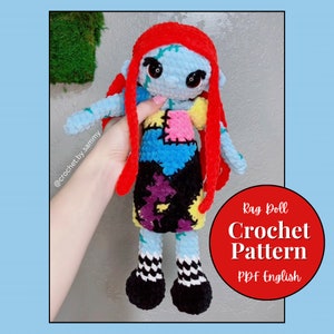 Op de afbeelding: Een haakpatroon voor een lappop met rood haar, een blauw-gele patchworkjurk en zwart-wit geblokte schoenen. Het patroon is beschikbaar in PDF-formaat en is geschreven in het Engels. De tekst op de afbeelding luidt "Rag Doll Crochet Pattern PDF English".