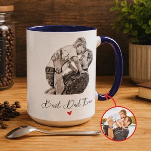 May include: White ceramic mug with a blue interior and handle, featuring a sketch of a father and child. The mug has the text "Best Dad Ever" and a small red heart. A small photo of a father and child is also included.