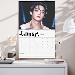 May include: A wall calendar for January 2026 featuring a portrait of a person. The calendar has a white background with a grid layout for the days. The word "January" is written in a bold, stylized font.