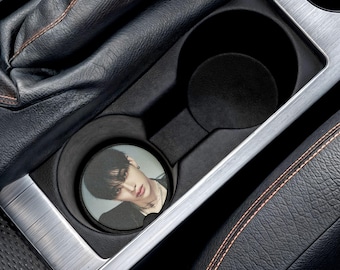 Könnte beinhalten: Ein runder Untersetzer mit einem Schwarzweißfoto einer Person. Der Untersetzer befindet sich in einem Getränkehalter im Auto.