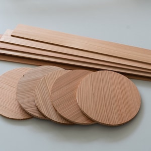 Puede incluir: Un conjunto de posavasos de madera y tablas rectangulares. Los posavasos son redondos con varios patrones de vetas de madera. Las tablas son largas y rectangulares, todas en un tono de madera natural. Los artículos están dispuestos sobre una superficie gris claro.