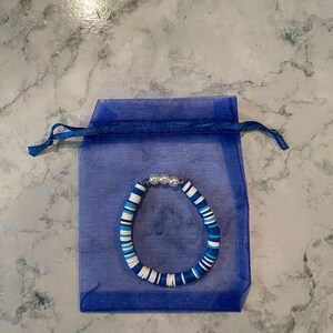 May include: A blue and white beaded bracelet with white pearl accents, displayed in a blue organza bag.