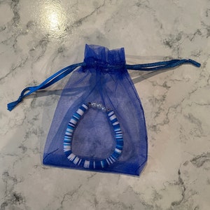 May include: A blue and white striped bracelet with white beads, packaged in a blue organza bag.