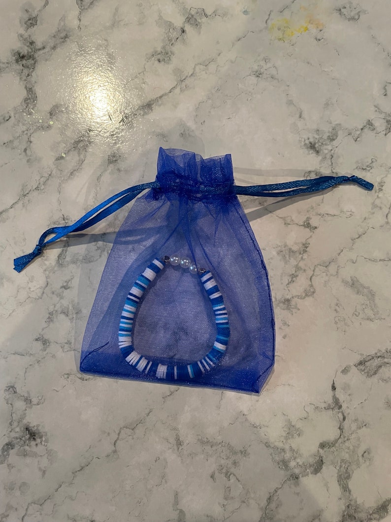 May include: A blue and white striped bracelet with white beads, packaged in a blue organza bag.