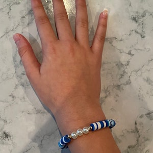 May include: A blue and white striped bracelet with three white pearl beads.