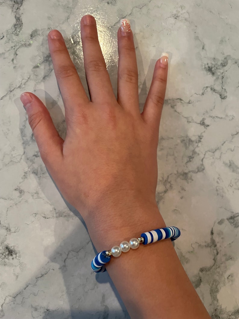 May include: A blue and white striped bracelet with three white pearl beads.
