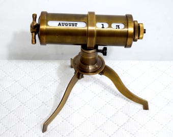 May include: A brass telescope-style calendar with a tripod stand. The calendar displays the month "AUGUST" and the date "13".