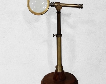 May include: A vintage-style magnifying glass on a wooden base. The brass-colored frame holds a circular lens. The adjustable stand is brass and dark wood, with a round wooden base. The magnifying glass is designed for detailed viewing.