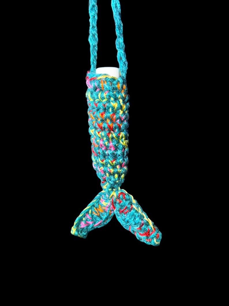 May include: A turquoise crochet lip balm holder with a mermaid tail design. The holder is made of colorful yarn with pink, yellow, and red accents. The holder has a turquoise strap for carrying.