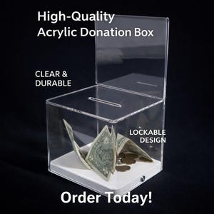 May include: A clear acrylic donation box with a slot on top and a lockable design. The box contains paper money and coins. Text on the box reads "High-Quality Acrylic Donation Box", "Clear & Durable", "Lockable Design", and "Order Today!"