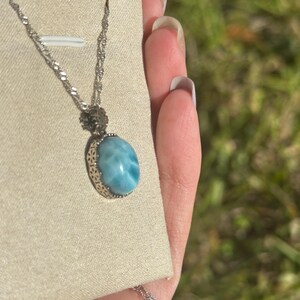 Pode incluir: Um colar de corrente de prata com um pingente oval azul e branco com um padr&atilde;o de redemoinho. O pingente &eacute; engastado em uma moldura de filigrana de prata.