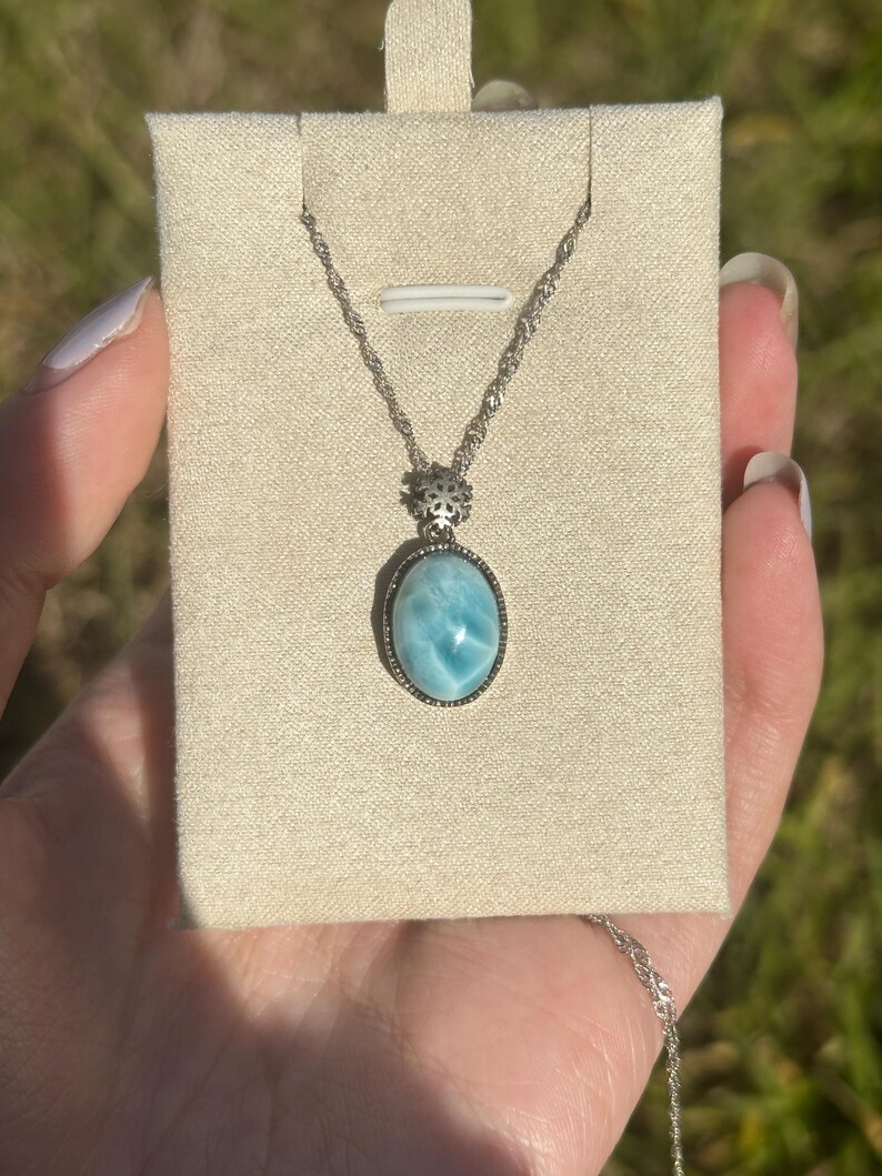 Pode incluir: Um colar de corrente de prata com um pingente oval azul que apresenta uma pedra preciosa com um padr&atilde;o de m&aacute;rmore. O pingente &eacute; engastado em uma moldura de prata com um design decorativo.