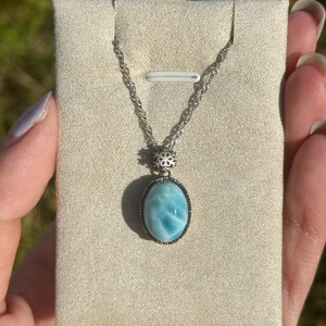 Pode incluir: Um colar de corrente de prata com um pingente oval azul e branco engastado em uma moldura de prata. O pingente &eacute; uma pedra preciosa com um padr&atilde;o de redemoinho.