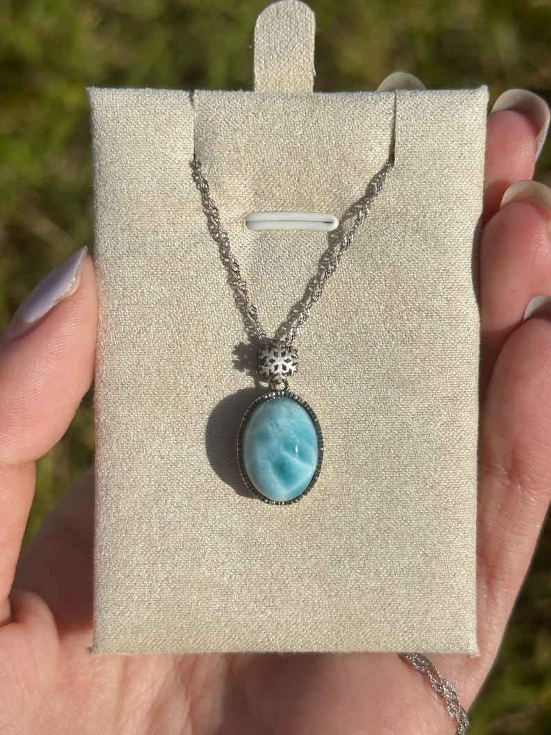 Pode incluir: Um colar de corrente de prata com um pingente oval azul e branco engastado em uma moldura de prata. O pingente &eacute; uma pedra preciosa com um padr&atilde;o de redemoinho.