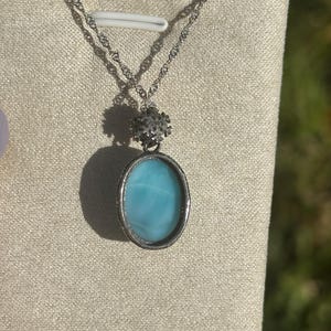 Pode incluir: Um colar de corrente de prata com um pingente oval azul e um charme de floco de neve prateado.