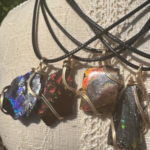 以下が含まれることがあります： 金色のワイヤーで包まれた虹色の宝石のペンダントが4つ、それぞれ黒いコードネックレスからぶら下がっています。宝石は濃い青、緑、赤が混ざっています。