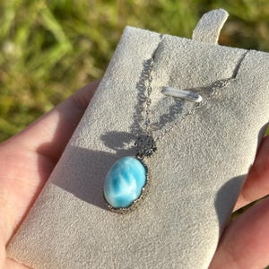 Pode incluir: Um colar de corrente de prata com um pingente oval azul e branco. O pingente &eacute; engastado em uma moldura de prata e tem um design delicado e intrincado.