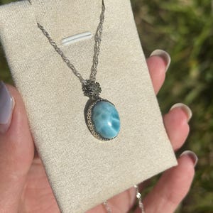 Pode incluir: Um colar de corrente de prata com um pingente oval azul e branco engastado em uma moldura de filigrana de prata.