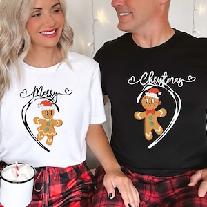 Può includere: T-shirt bianche e nere con disegni di omini di pan di zenzero abbinati. La maglietta bianca dice "Merry" sopra un omino di pan di zenzero con un cappello da Babbo Natale. La maglietta nera dice "Christmas" sopra un omino di pan di zenzero abbinato.