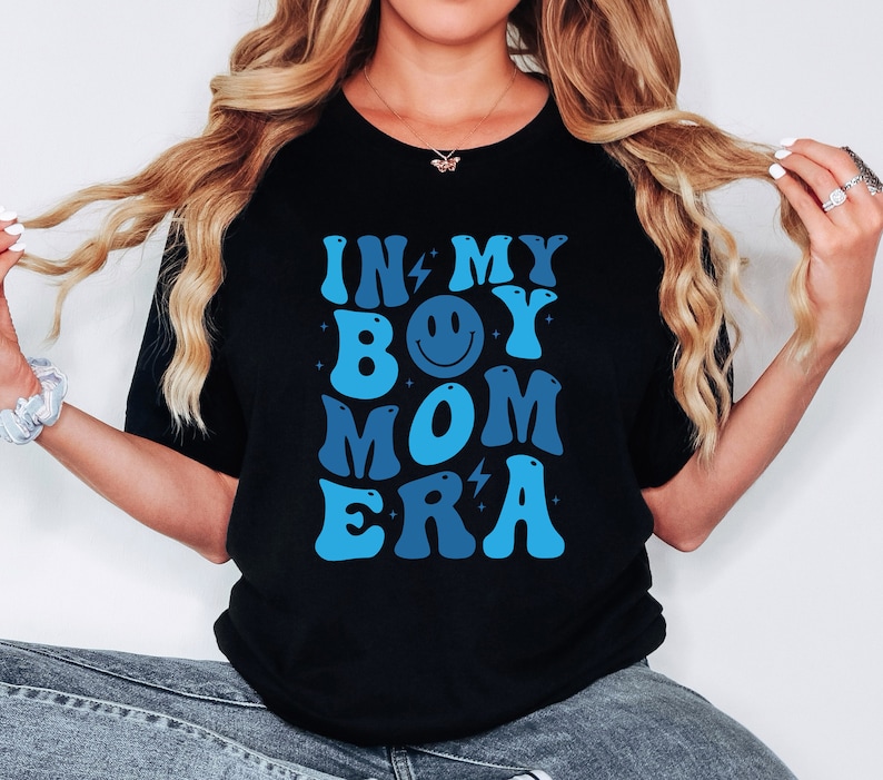 May include: Black t-shirt with a blue and white graphic that says "In My Boy Mom Era" with a smiley face in the middle.