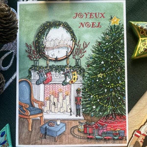 Op de afbeelding: Een kerstkaart met de tekst "JOYEUX NOEL" in het rood. De illustratie toont een versierde kerstboom, een open haard met kousen en een spiegel die een winterse scène weerspiegelt. Een blauwe stoel en cadeaus zijn ook zichtbaar.