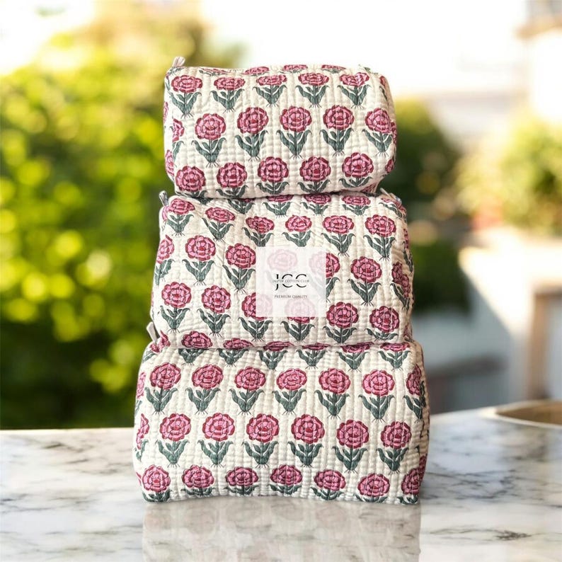 May include: Three stackable quilted cotton makeup bags with a pink floral print. The bags are made by JCC, a brand of handmade goods.