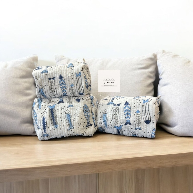 May include: Three white quilted zippered pouches with a blue and white fish pattern. The pouches are stacked on top of each other on a wooden surface.