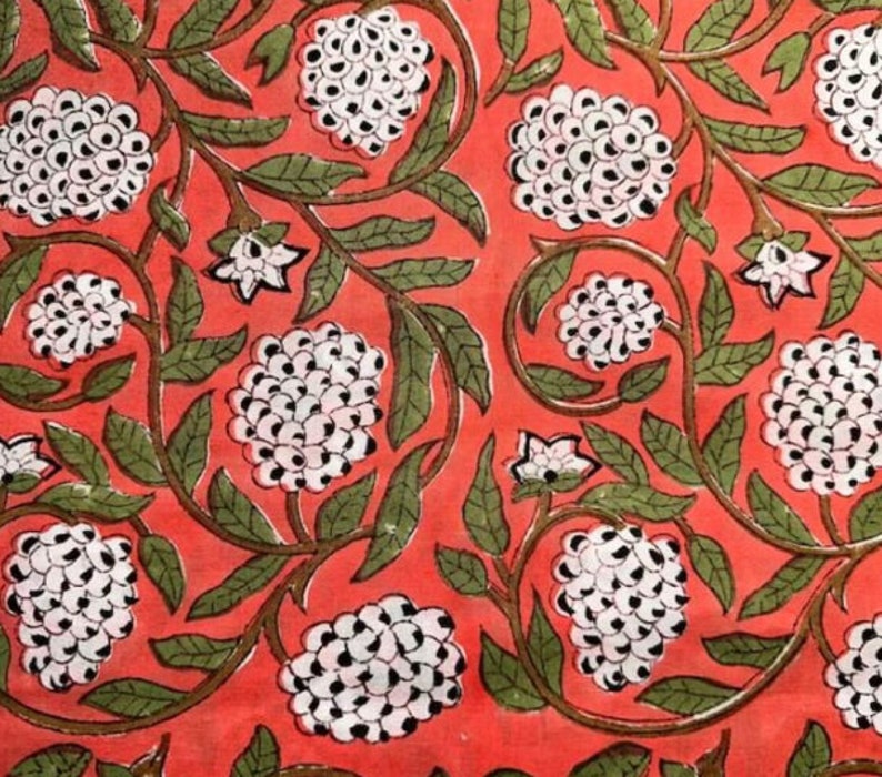Puede incluir: Una tela roja con un patr&oacute;n repetitivo de flores blancas con centros negros. Las flores est&aacute;n dispuestas en vides verdes.