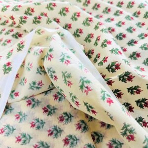 Puede incluir: Tela de color crema con un patr&oacute;n repetido de peque&ntilde;as hojas verdes y flores rojas.