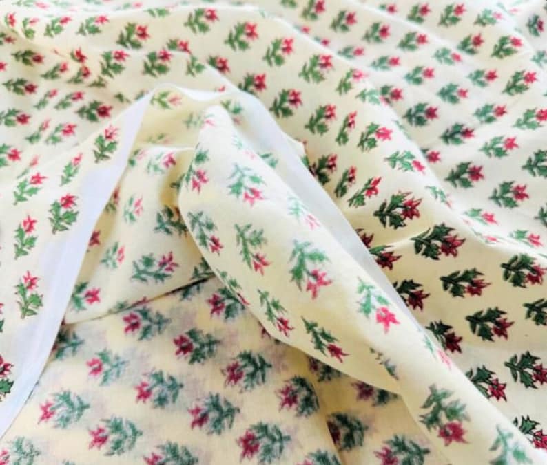 Puede incluir: Tela de color crema con un patr&oacute;n repetido de peque&ntilde;as hojas verdes y flores rojas.