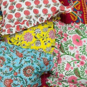 Puede incluir: Cuatro almohadas decorativas con patrones florales. Las almohadas est&aacute;n hechas de tela de algod&oacute;n y tienen un borde con volantes. Las almohadas est&aacute;n apiladas, con la almohada superior siendo blanca con flores rojas, la segunda almohada siendo amarilla con flores rosas y blancas, la tercera almohada siendo azul con flores rosas y la almohada inferior siendo blanca con flores rosas.