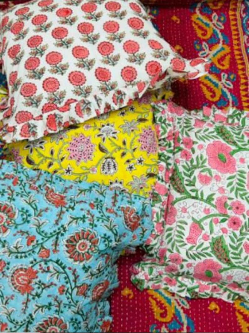 Puede incluir: Cuatro almohadas decorativas con patrones florales. Las almohadas est&aacute;n hechas de tela de algod&oacute;n y tienen un borde con volantes. Las almohadas est&aacute;n apiladas, con la almohada superior siendo blanca con flores rojas, la segunda almohada siendo amarilla con flores rosas y blancas, la tercera almohada siendo azul con flores rosas y la almohada inferior siendo blanca con flores rosas.