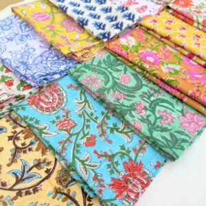 Puede incluir: Una colecci&oacute;n de 10 servilletas de algod&oacute;n de colores con motivos florales. Las servilletas est&aacute;n dobladas y dispuestas en fila. Los motivos incluyen flores azules, verdes, amarillas, rosas y naranjas.