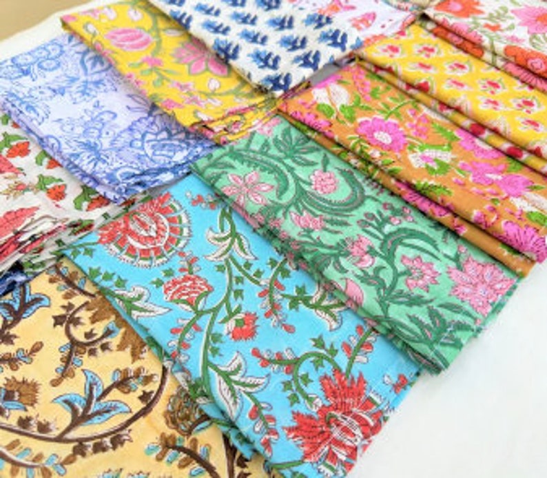 Puede incluir: Una colecci&oacute;n de 10 servilletas de algod&oacute;n de colores con motivos florales. Las servilletas est&aacute;n dobladas y dispuestas en fila. Los motivos incluyen flores azules, verdes, amarillas, rosas y naranjas.