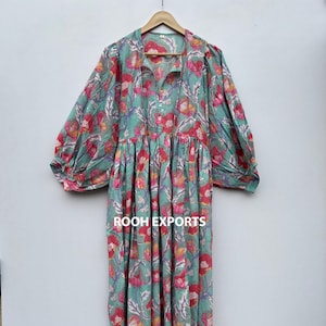Puede incluir: Un vestido largo y fluido con un estampado floral en tonos turquesa, rosa y rojo. El vestido presenta un cuello camisero, una botonadura frontal y mangas largas y voluminosas. El texto "ROOH EXPORTS" es visible.