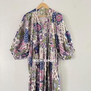 Könnte beinhalten: Ein langes, fließendes Kleid mit Patchwork-Design. Das Kleid hat einen V-Ausschnitt, lange Ärmel und einen Stufenrock. Der Stoff ist weiß mit einem Blumenmuster in Rosa, Blau, Grün und Lila. Der Text "ROOH EXPORTS" ist sichtbar.