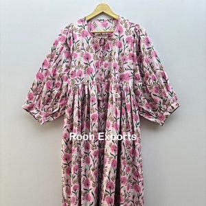 May include: A pink floral print dress with long, puffy sleeves and a tie-neck detail. The dress features a repeating pattern of pink flowers and green leaves on a light pink background. The text "Rooh Exports" is visible on the dress.