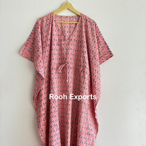 Puede incluir: Una kaftán de algodón rosa con estampado floral y un lazo en la cintura. La kaftán tiene mangas cortas y cuello en V. El texto "Rooh Exports" está impreso en la parte delantera de la kaftán.