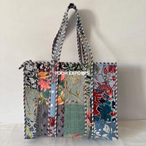 Può includere: Una borsa tote patchwork con una varietà di motivi floreali e geometrici nei toni del blu, verde, rosso e arancione. La borsa ha una chiusura con cerniera e manici abbinati. Il testo "ROOH EXPORTS" è visibile.